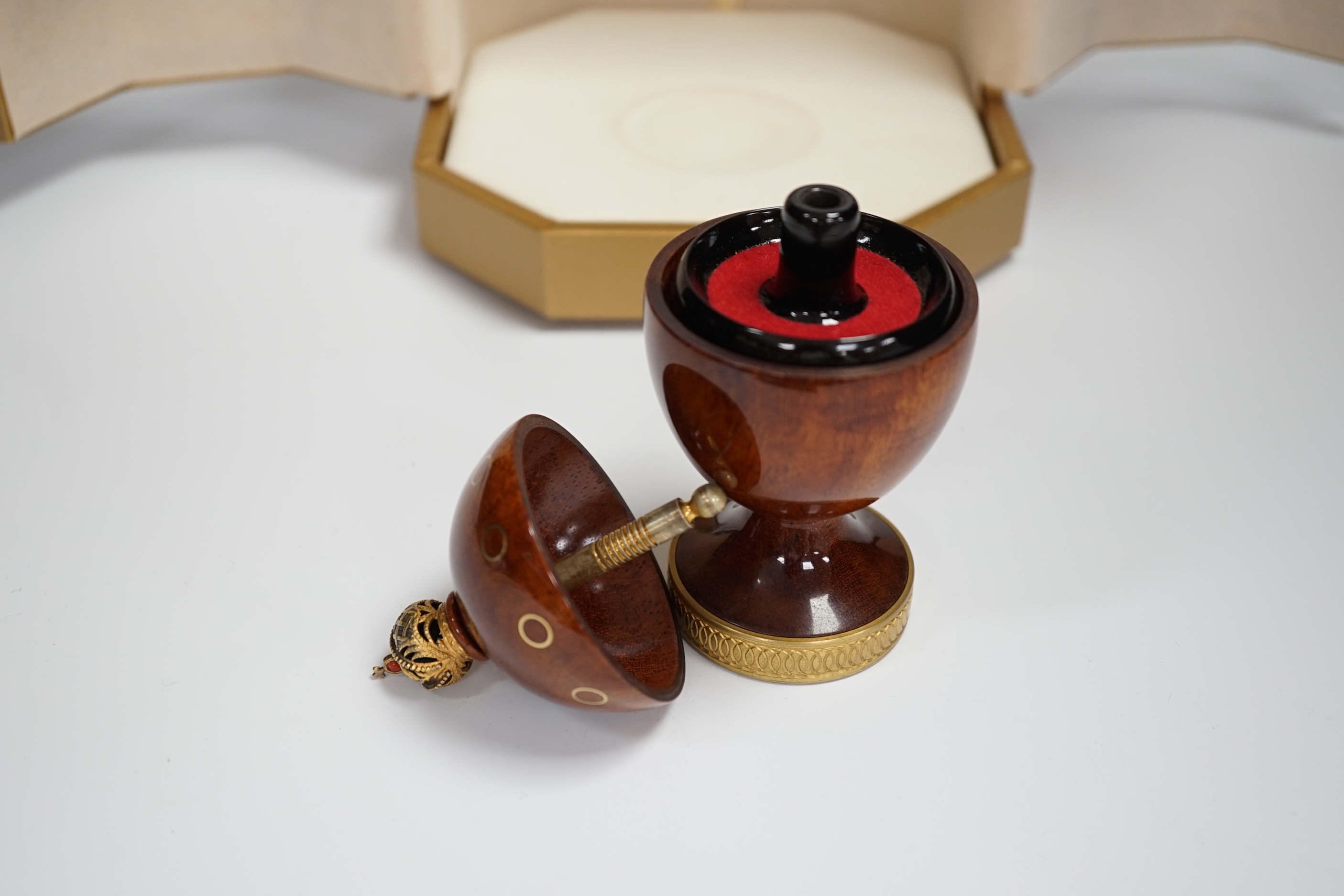 A cased Theo Faberge, (1922-2007) turned bubinga wood Eternity Egg, with Imperial Crown finial, gilt ring decoration and interior blackwood ring tray, with box and paperwork, 13.1cm